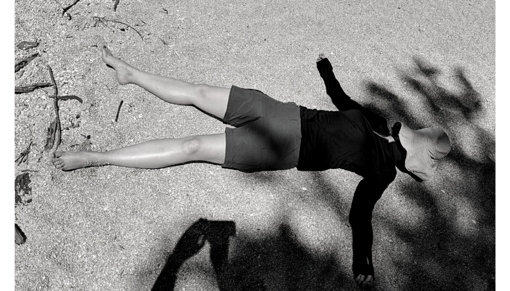 woman lying down in the sand with hat on her face